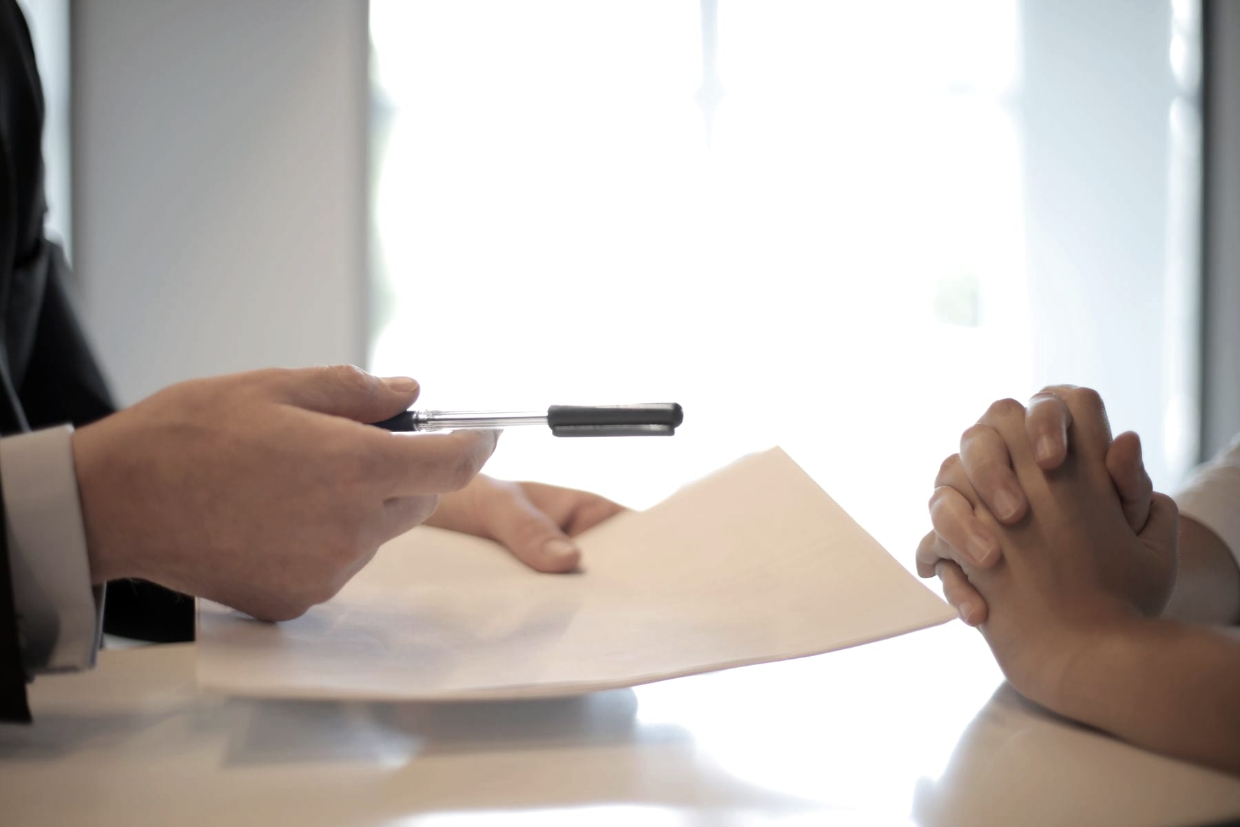 One person passing a printed agreement across a desk to another
